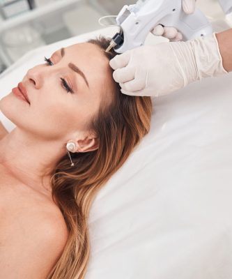 Top view of pretty female lying on couch while cosmetologist is doing injections in her head